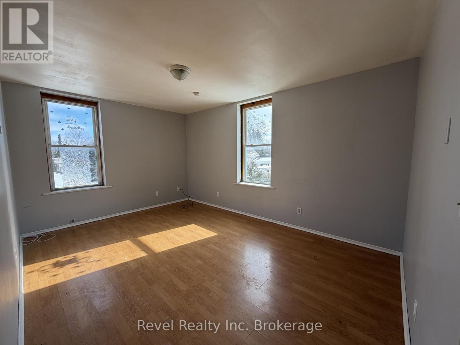 A room with wooden flooring and two windows, one of which has a view of a tree covered in snow.