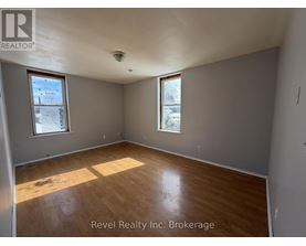 A room with wooden flooring and two windows, one of which has a view of a tree covered in snow.