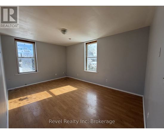 A room with wooden flooring and two windows, one of which has a view of a tree covered in snow.