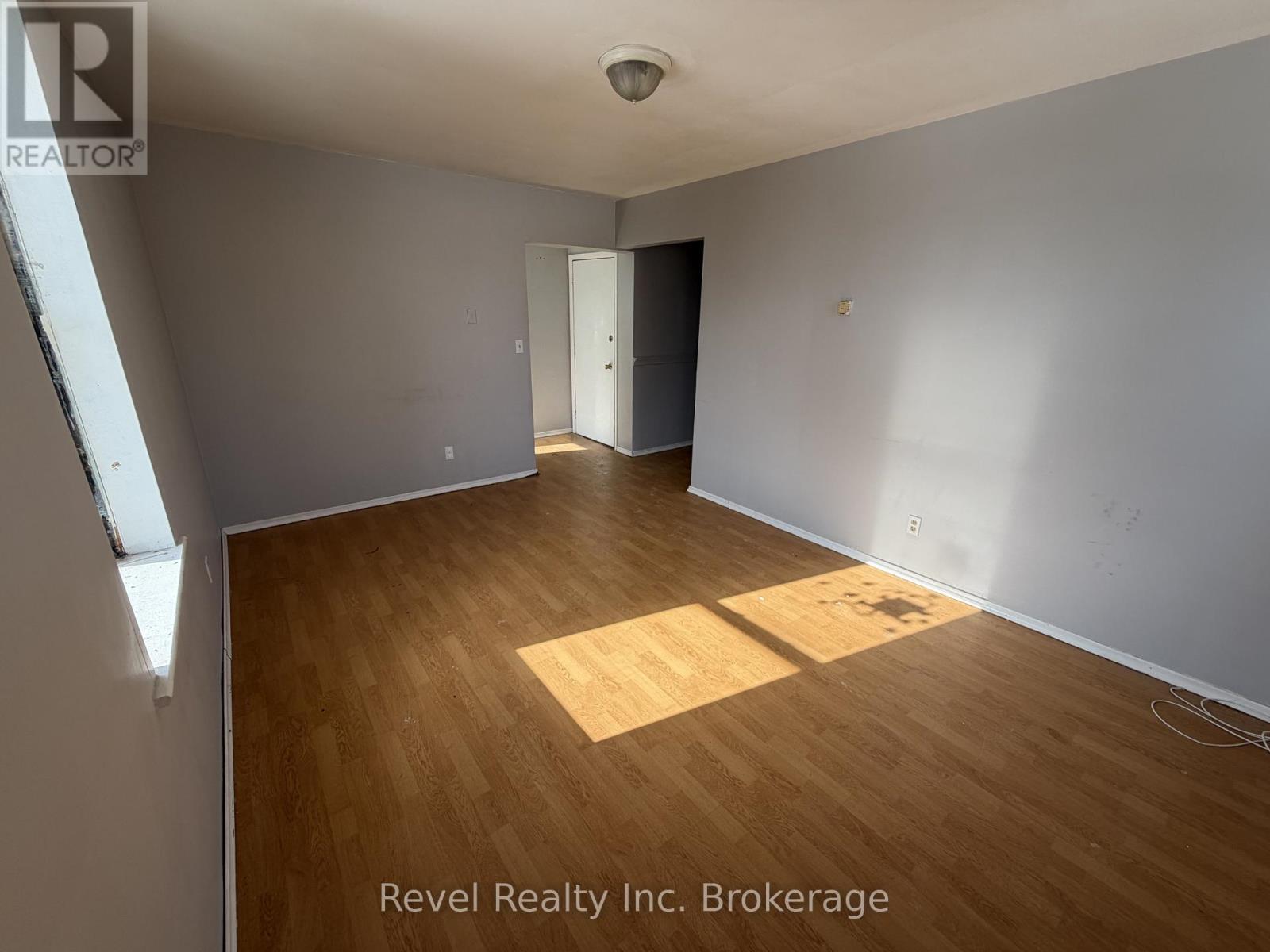A room with wooden flooring and white walls, with a door on the right side.