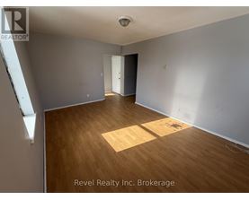 A room with wooden flooring and white walls, with a door on the right side.
