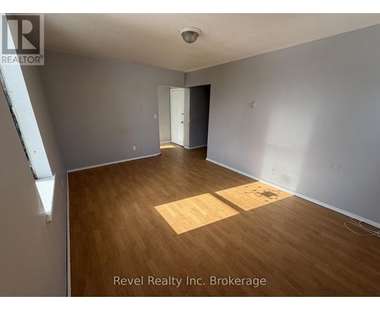 A room with wooden flooring and white walls, with a door on the right side.