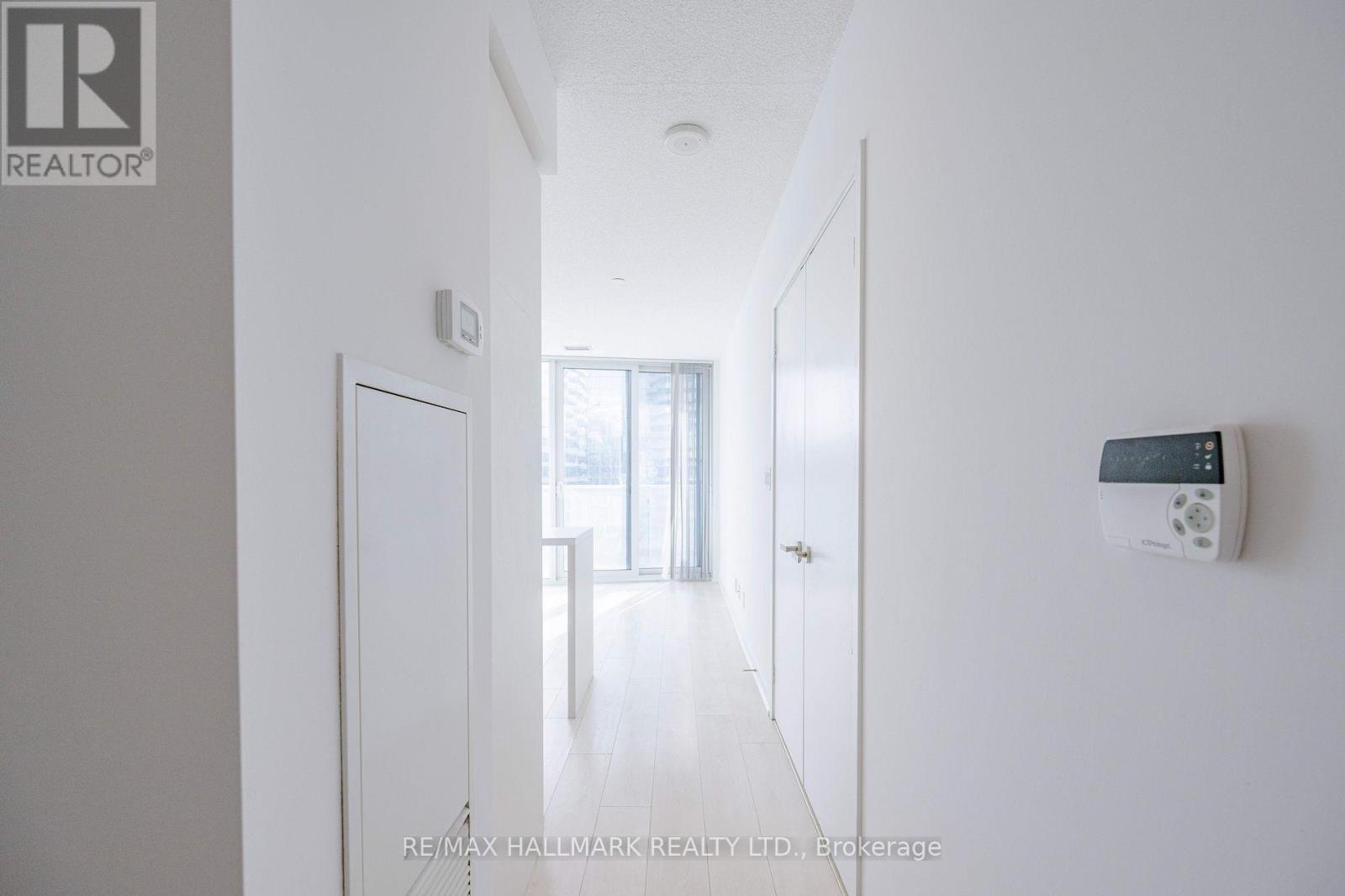 A hallway with a door on the left and a thermostat on the wall.