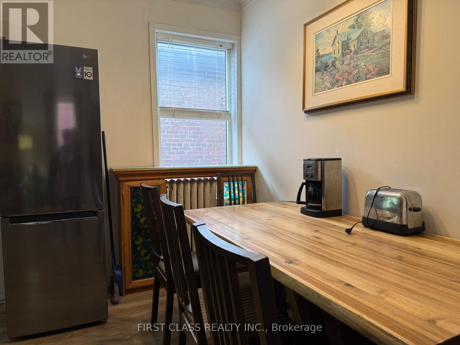 A kitchen with a wooden table and chairs, a refrigerator, and a window.