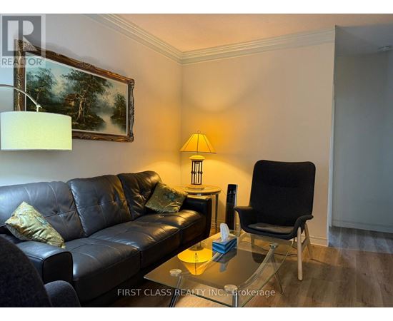 A black leather couch sits in a living room with a lamp and a painting on the wall.