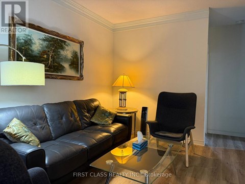 A black leather couch sits in a living room with a lamp and a painting on the wall.