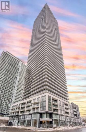 A tall building with a pointed top is in the foreground with a sunset in the background.
