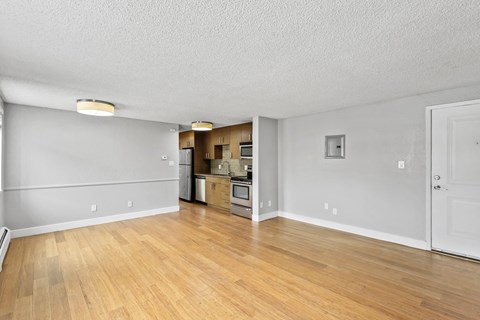 A room with wooden floors and a kitchen area in the background.