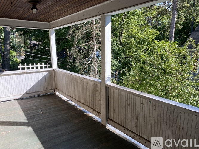 A wooden deck with a white railing and a view of trees and a fence.
