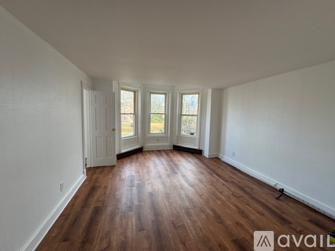 A room with wooden floors and white walls, with a door and three windows.