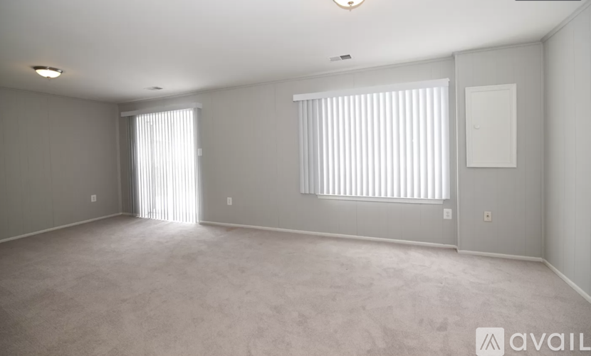 A spacious room with a carpeted floor and two windows with blinds.