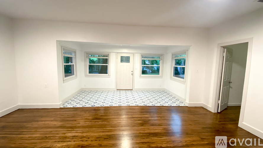 A room with wooden floors and white walls, featuring a door and two windows.
