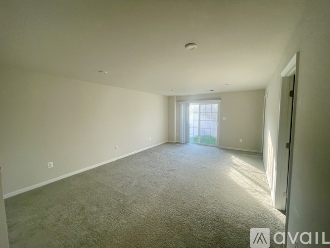 A spacious room with carpeted floor and a door leading to a window.