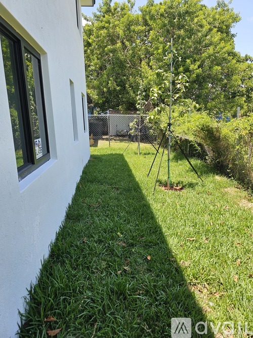 A white house with a green lawn and a tree in front of a fence.