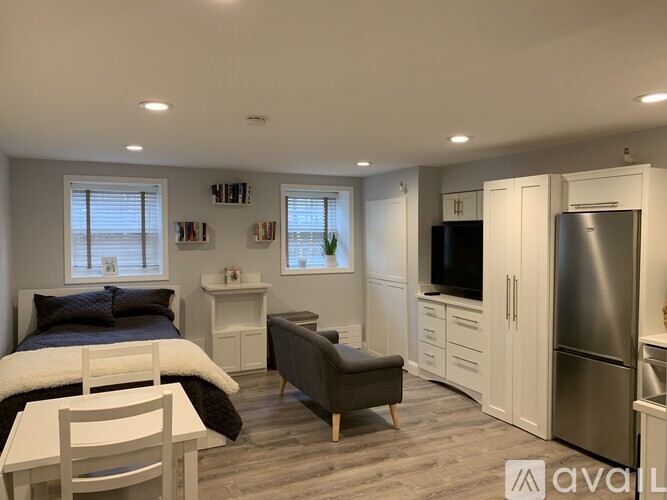 A modern bedroom with a large bed, a chair, a small table, and a refrigerator.