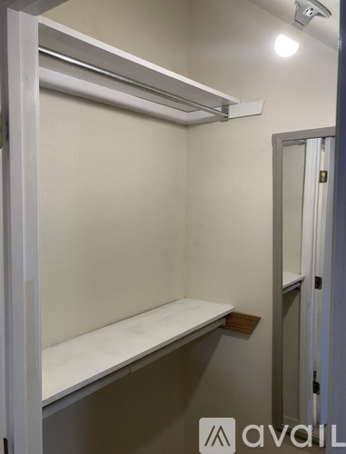A small, white, metal-framed closet with a shelf and a mirror.