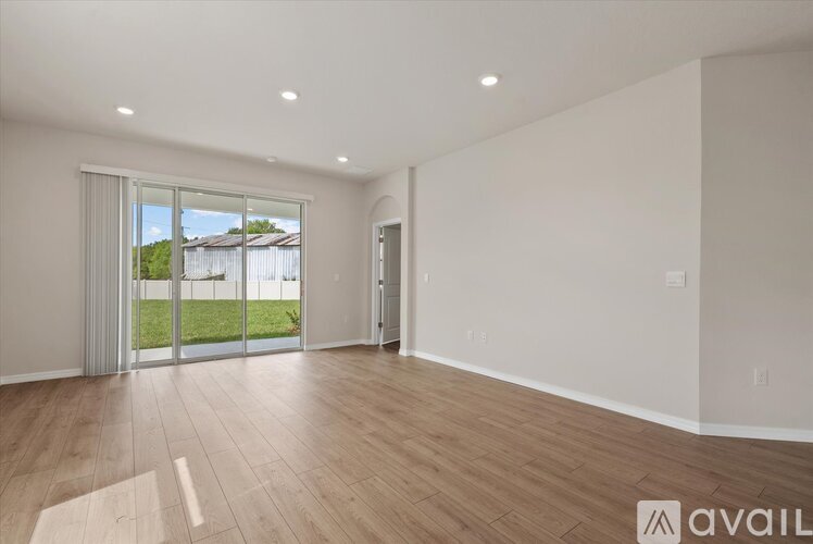 A spacious room with wooden flooring and a sliding glass door leading to a backyard.