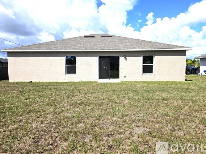 A small house with a grey roof and a black door is surrounded by a grassy area.