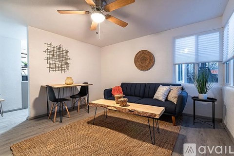 A living room with a blue couch, a wooden table, and a ceiling fan.