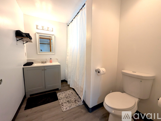 A white toilet sits in a small bathroom with a white shower curtain.