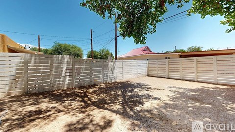 A backyard with a fence, a tree, and a house with a red roof in the background.