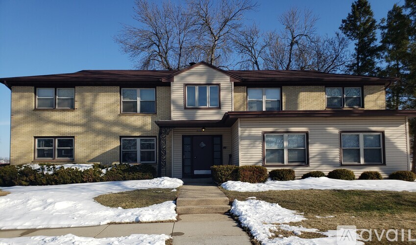 A house with a brown roof and beige siding is surrounded by snow.