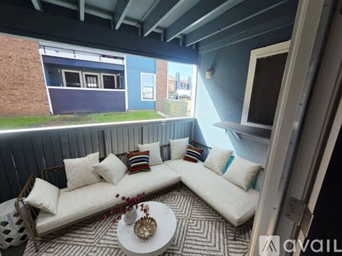 A white couch with colorful pillows sits on a patterned rug in a room with a balcony view.
