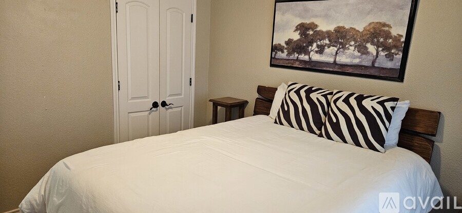 A bedroom with a white bed and a painting on the wall.