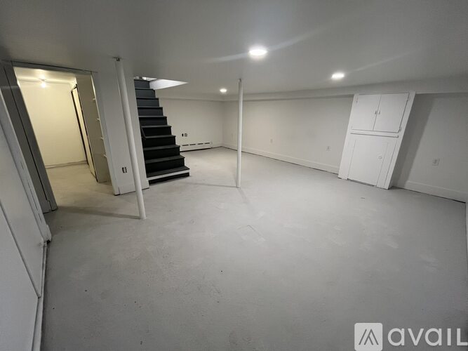 A spacious empty room with a staircase and a wall-mounted cabinet.