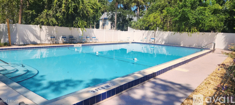 A large swimming pool surrounded by white fencing and trees.