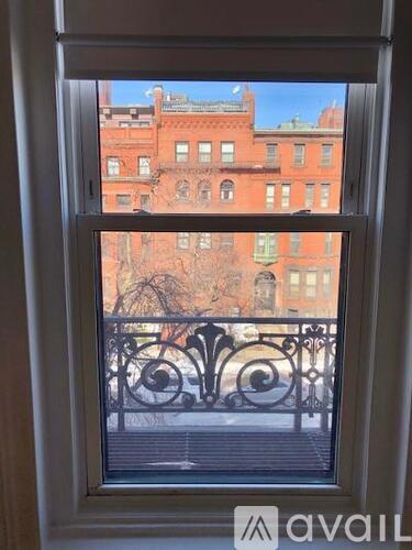 A window with a view of a red brick building and a black iron fence.