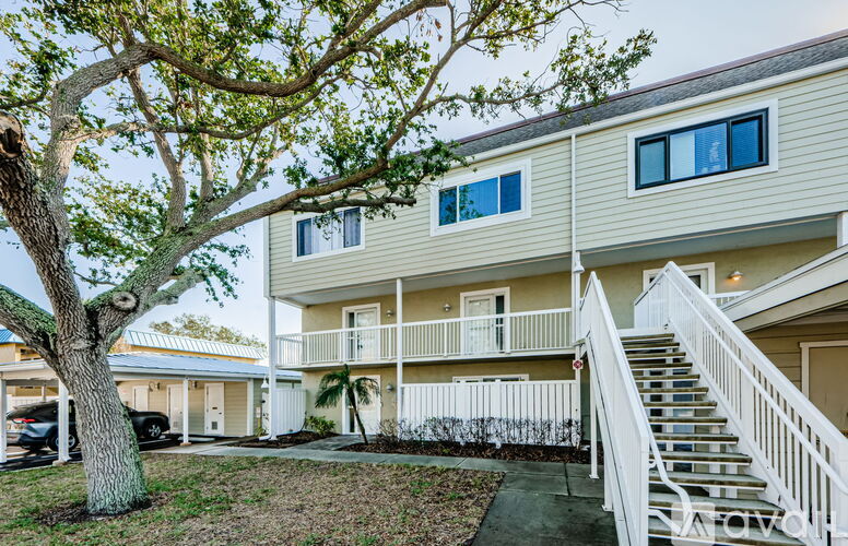 A tree is in front of a two-story building with a white railing on the stairs.