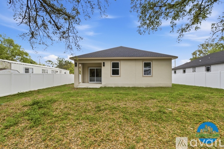 A small house with a brown roof is surrounded by a white fence and has a grassy yard.
