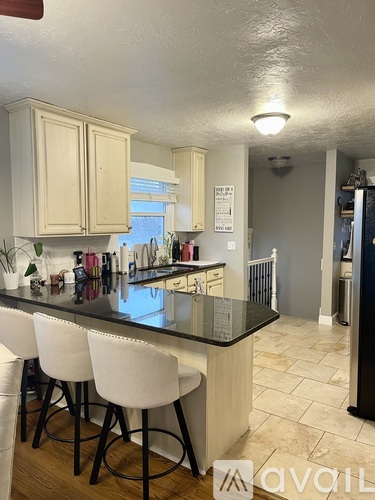 A kitchen with a black countertop and white chairs.