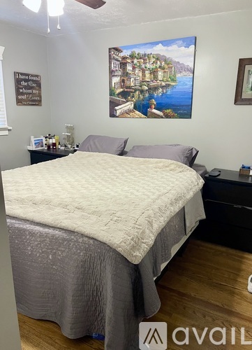 A bedroom with a bed, nightstand, and a painting on the wall.