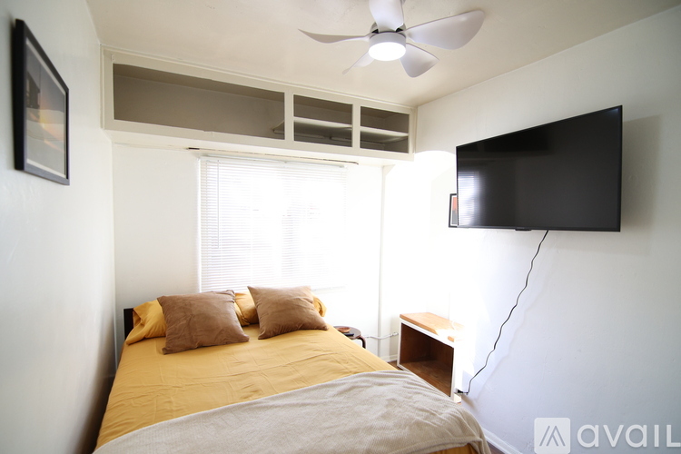 A bedroom with a bed, a ceiling fan, and a flat screen TV mounted on the wall.