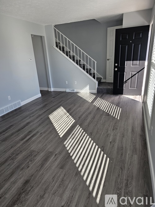 A room with a wooden floor and a staircase leading to the next floor.