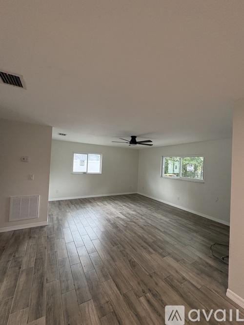 A spacious room with wooden flooring and two windows.
