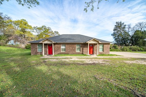 A house with a red door is surrounded by a grassy area.