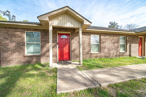 A red door is the centerpiece of this brick house.