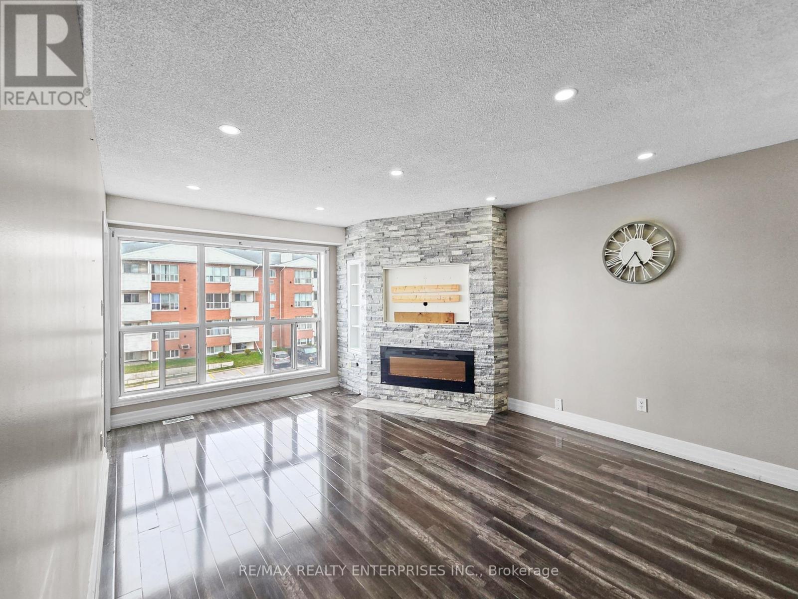 A spacious living room with a stone fireplace and a large window overlooking a building.