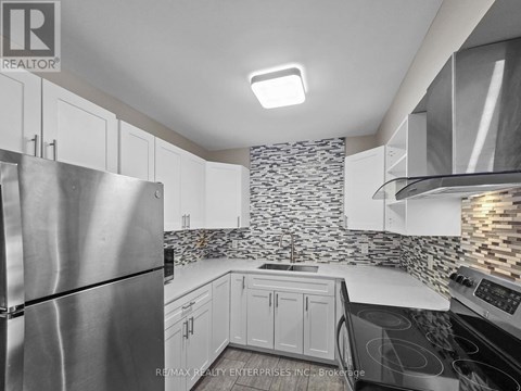 A kitchen with a stainless steel refrigerator and a stone backsplash.