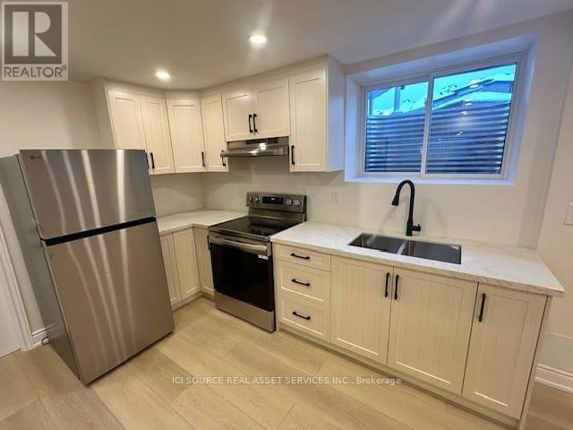 A kitchen with a stainless steel refrigerator, black oven, and white cabinets.