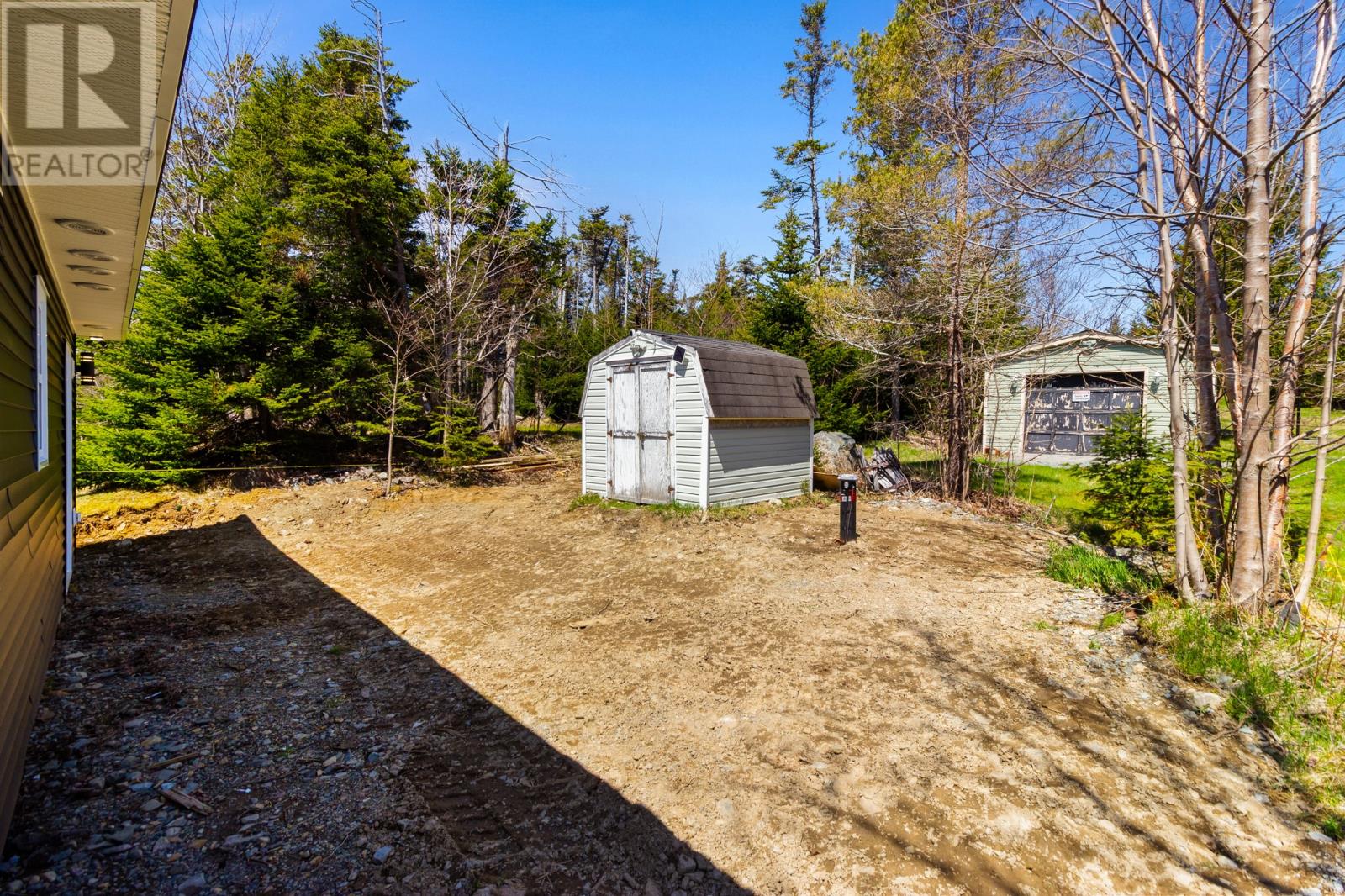 A dirt path leads to a small building in a wooded area.