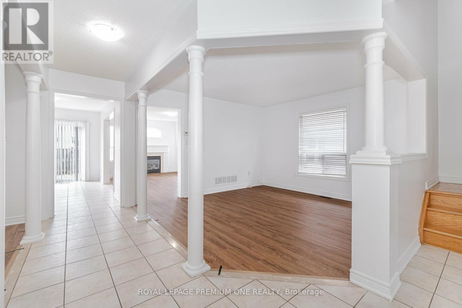 A spacious room with white walls and wooden flooring, featuring a series of white columns.