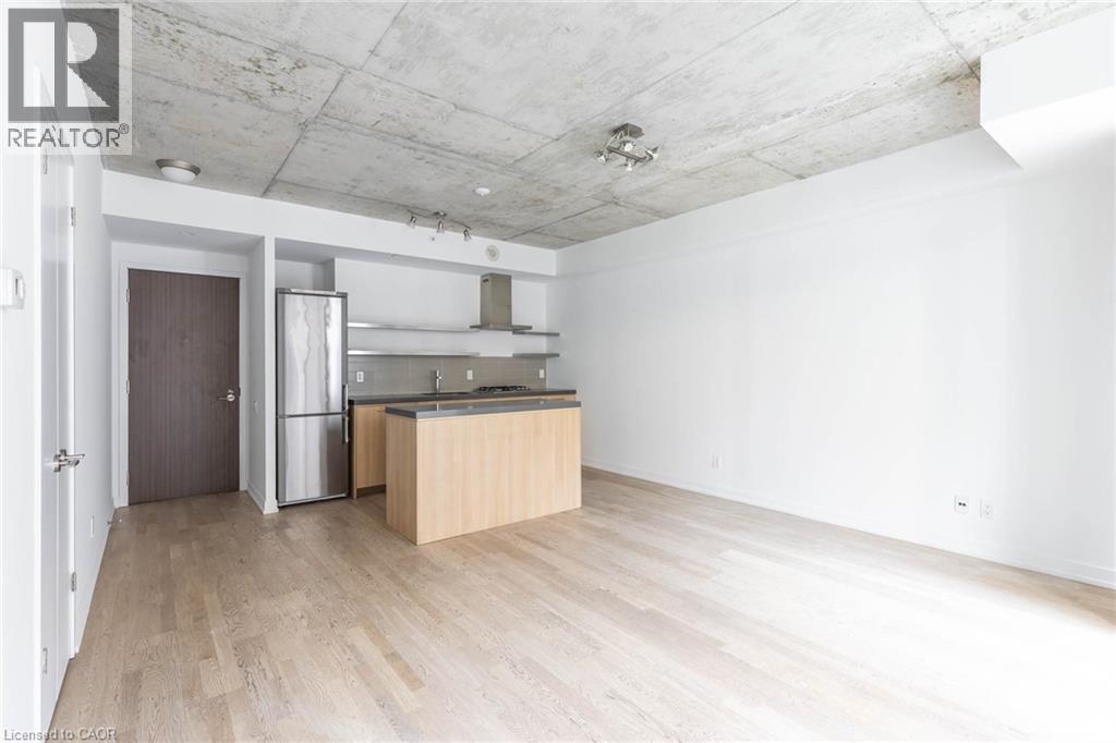 A spacious room with a wooden floor and a kitchen area with a refrigerator and a sink.