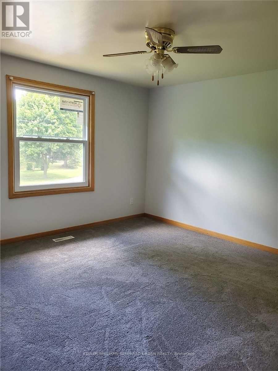 A room with a ceiling fan and a window showing trees outside.