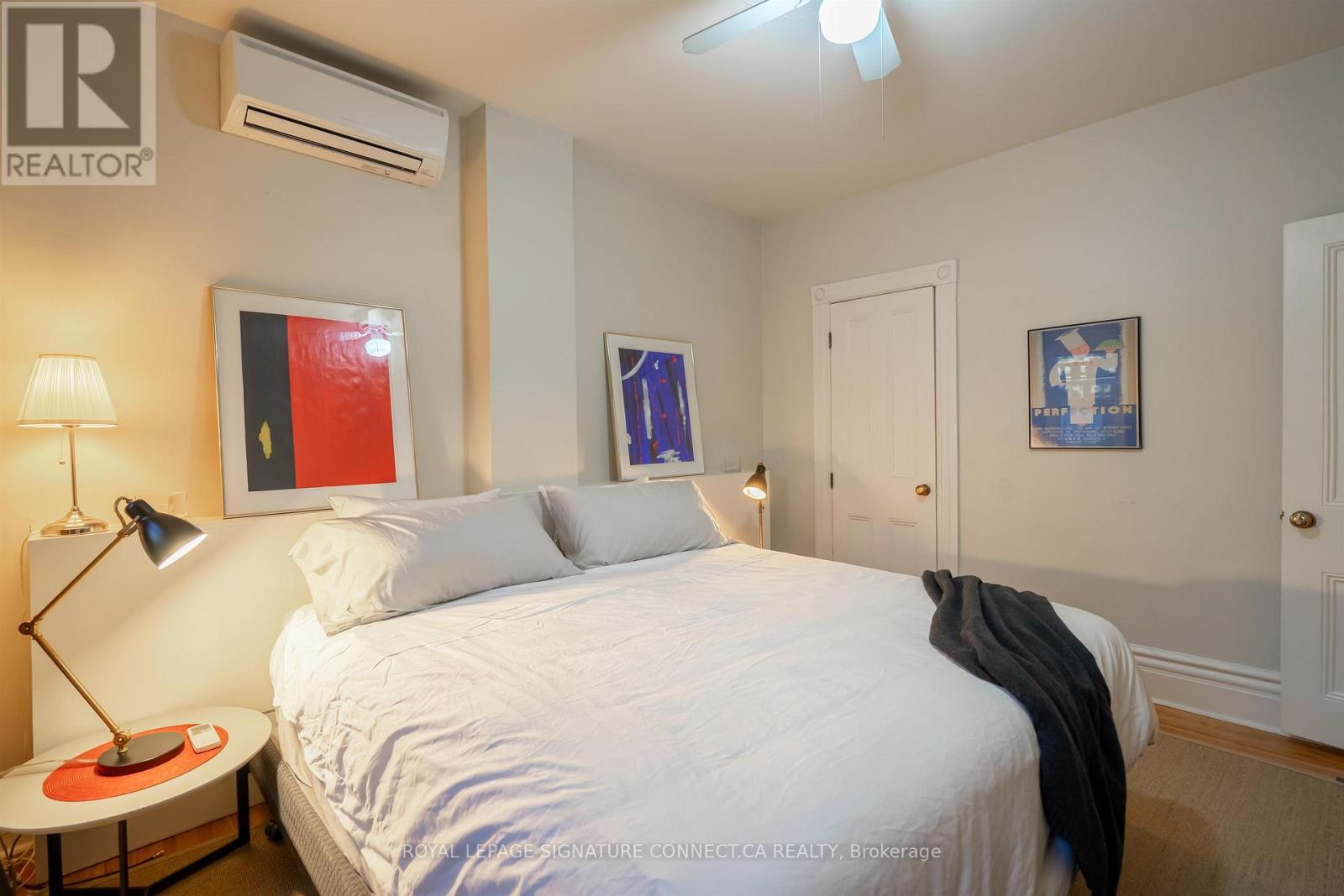 A bedroom with a white bed and a painting on the wall.
