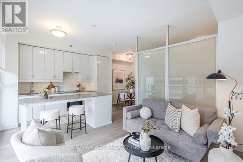 A modern living room with a grey couch and a kitchen area in the background.