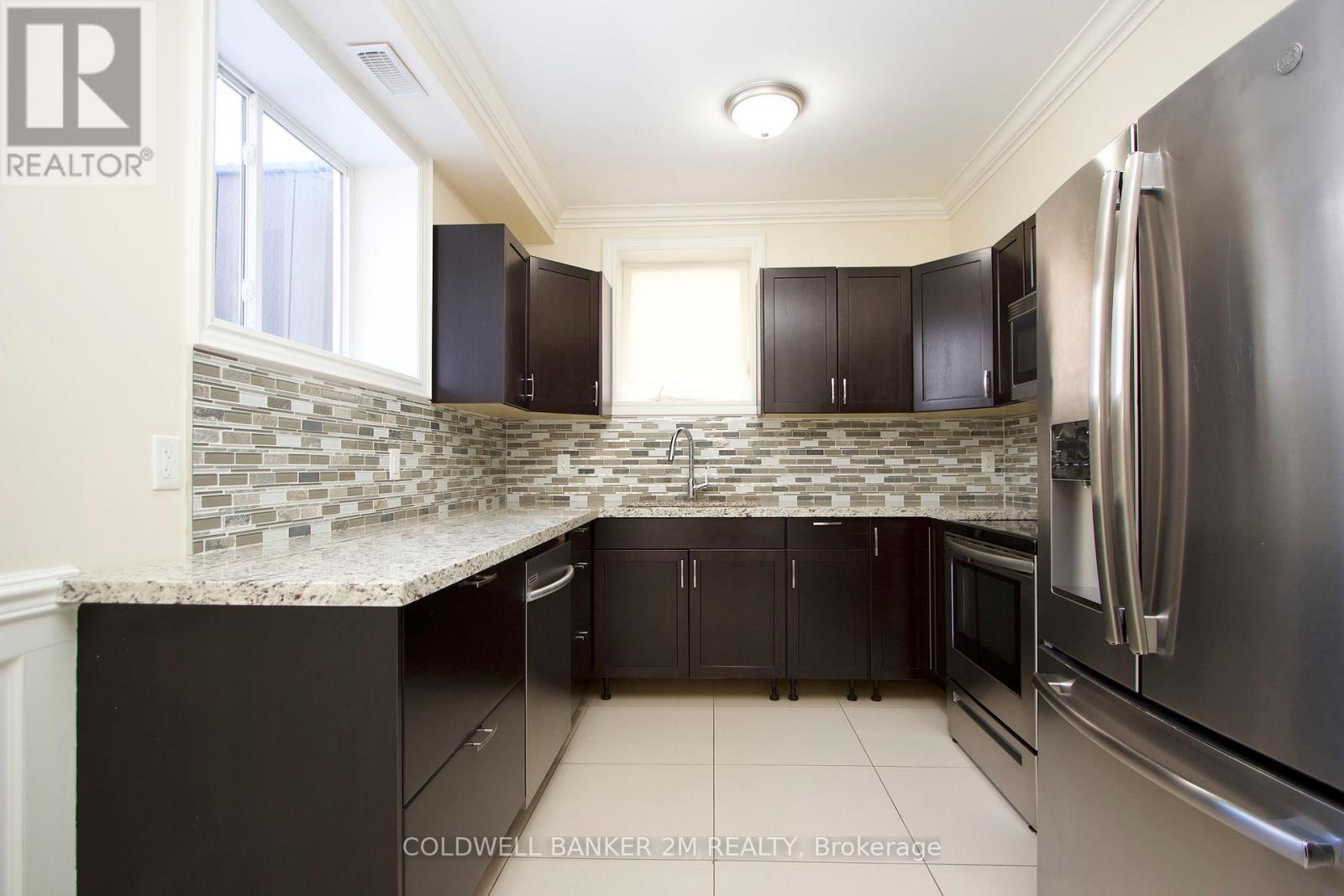 A kitchen with black cabinets and a stainless steel refrigerator.